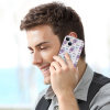Man talking on iPhone 13 with a white and purple patterned PC plastic case, protecting his phone.