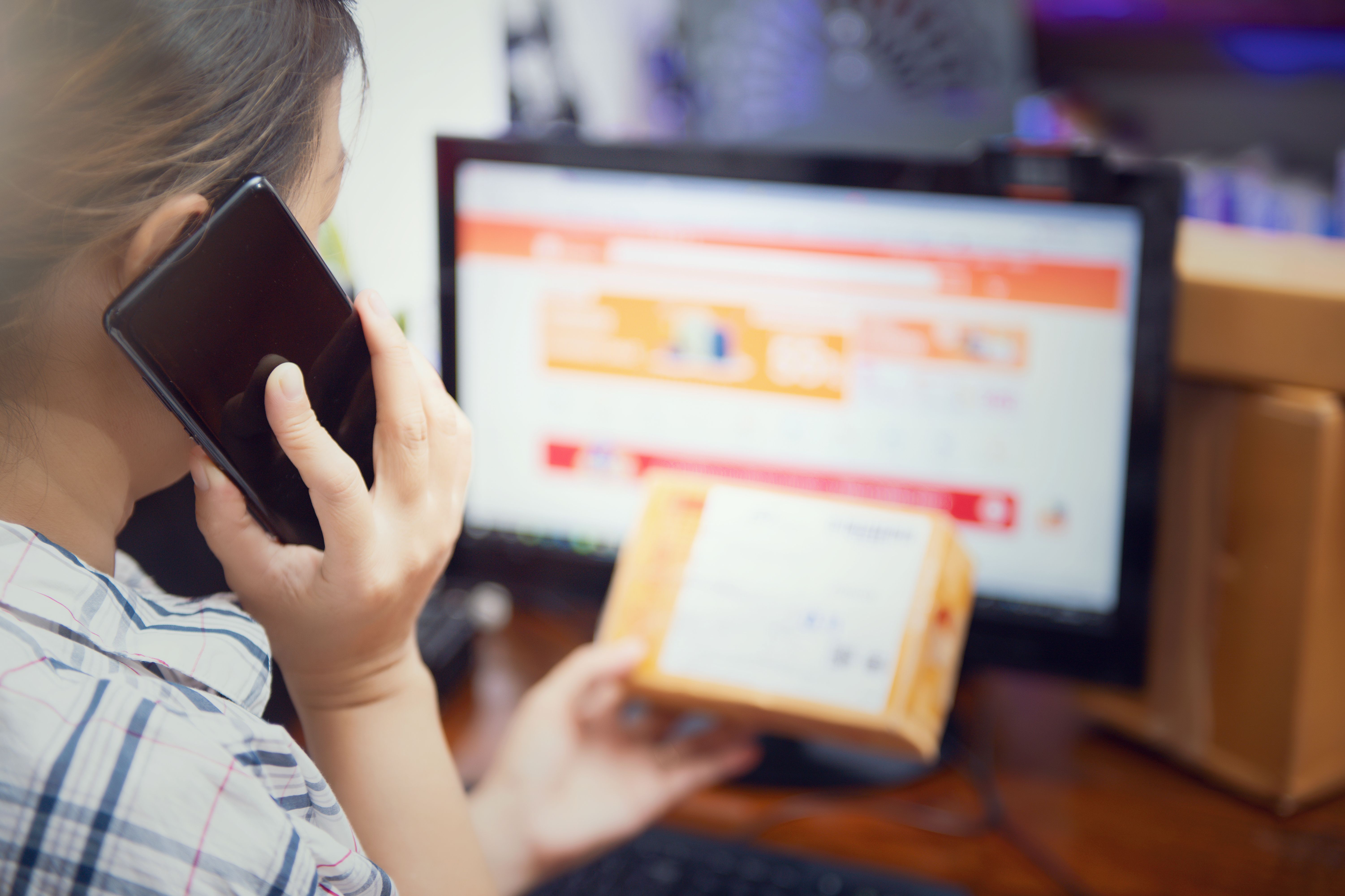 A product sourcing agent coordinating supplier orders by phone while inspecting a package at a desk.