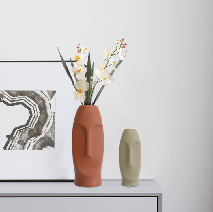 Terracotta and sage face vases with white orchids on a bright sideboard