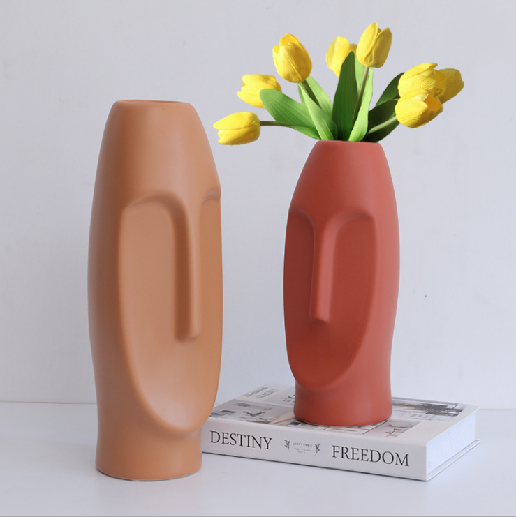 Two face vases beside yellow tulips on a styled stack of books