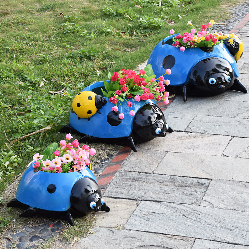 Blue ladybug planter with flowers standing on grass and stone paving
