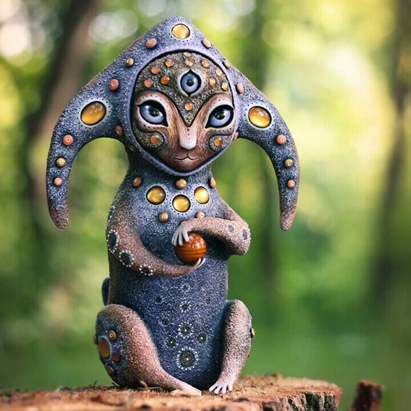 Blue-grey resin creature with amber jewel accents and an orange orb in its hands