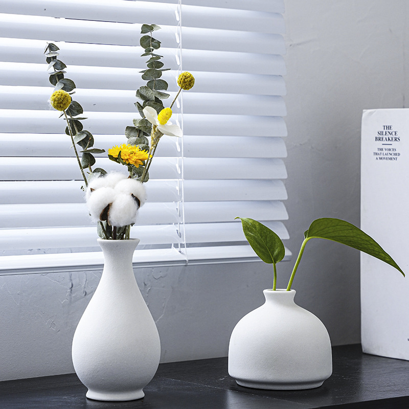 Two white matte ceramic vases on a windowsill with dried flowers and pothos