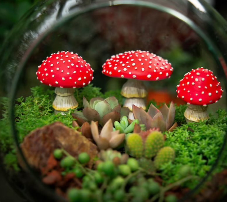Mushroom figurines in a glass terrarium with moss and succulents