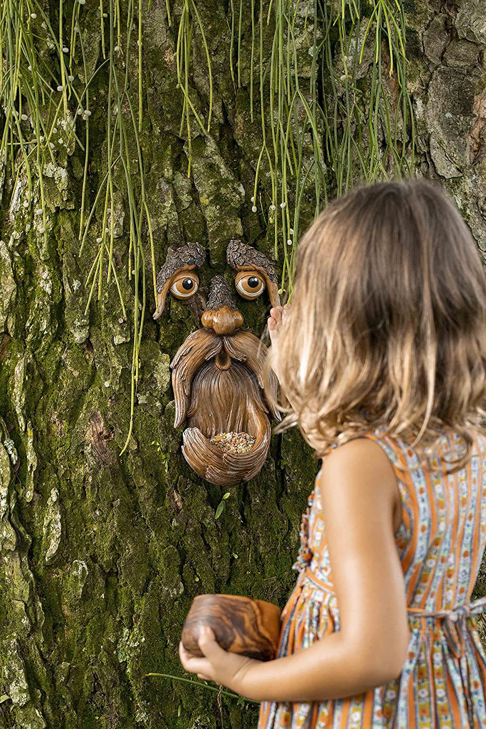Young girl looking up at the tree-face sculpture mounted on a trunk
