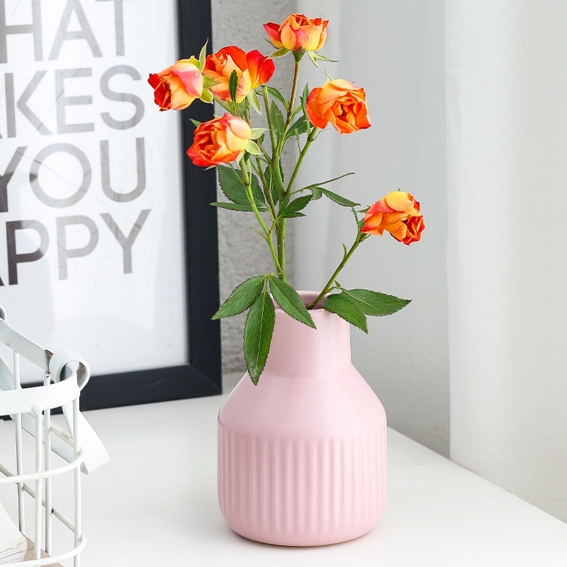 Blush pink ribbed vase holding orange roses on a white sideboard
