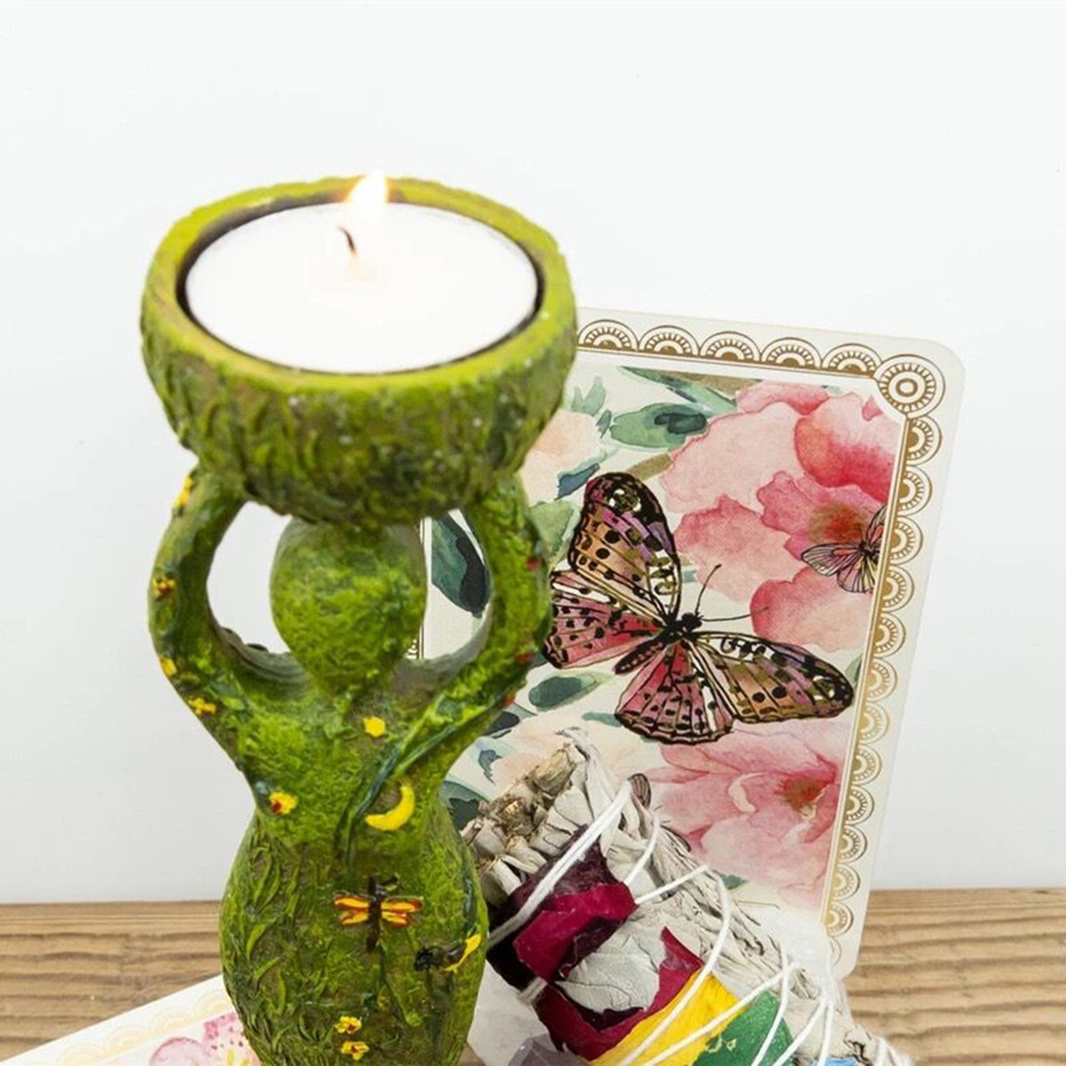 Lit tea light in green resin holder beside a tarot card on a wooden table