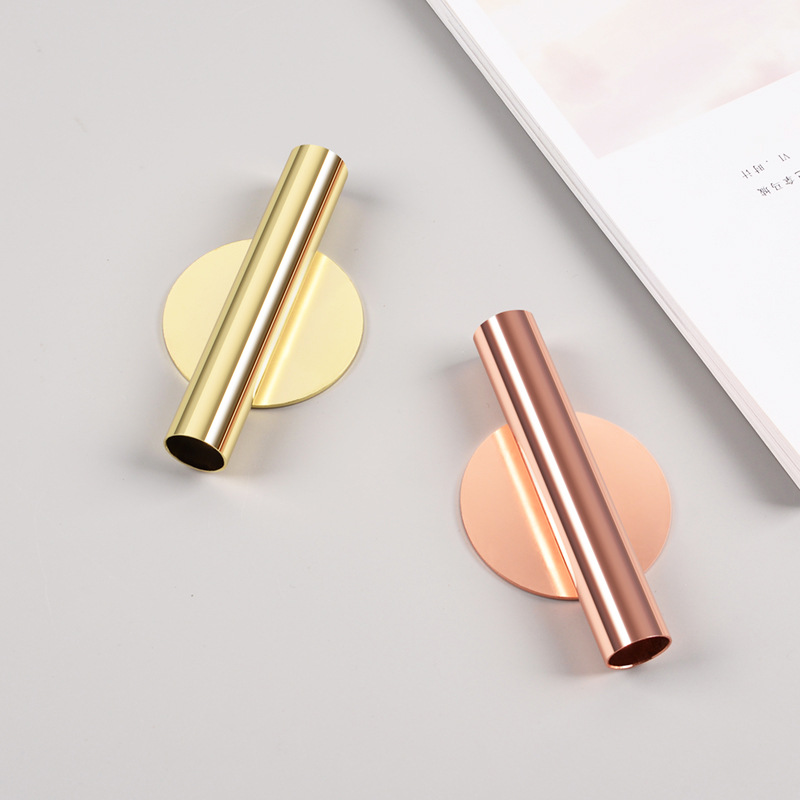 Gold and rose gold tube vase with round disc backplate beside a magazine