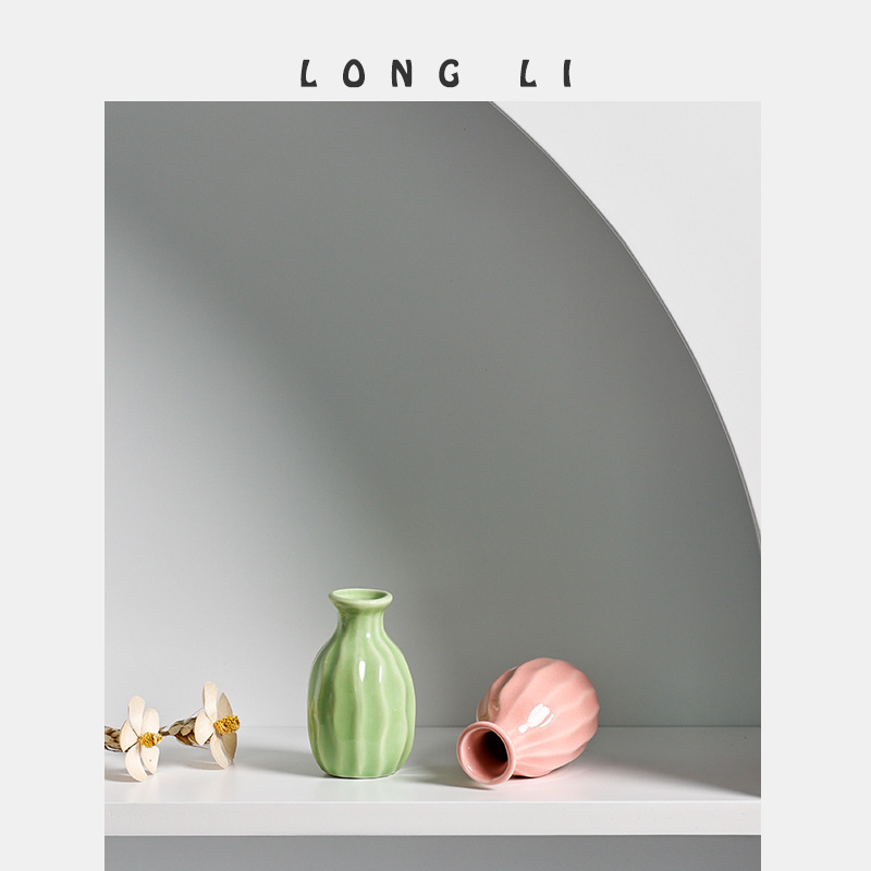 Pink mini ceramic vase tipped to show its open mouth beside dried stems