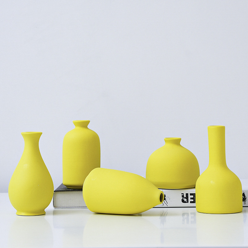 Five matte yellow ceramic bud vases in a row on a book