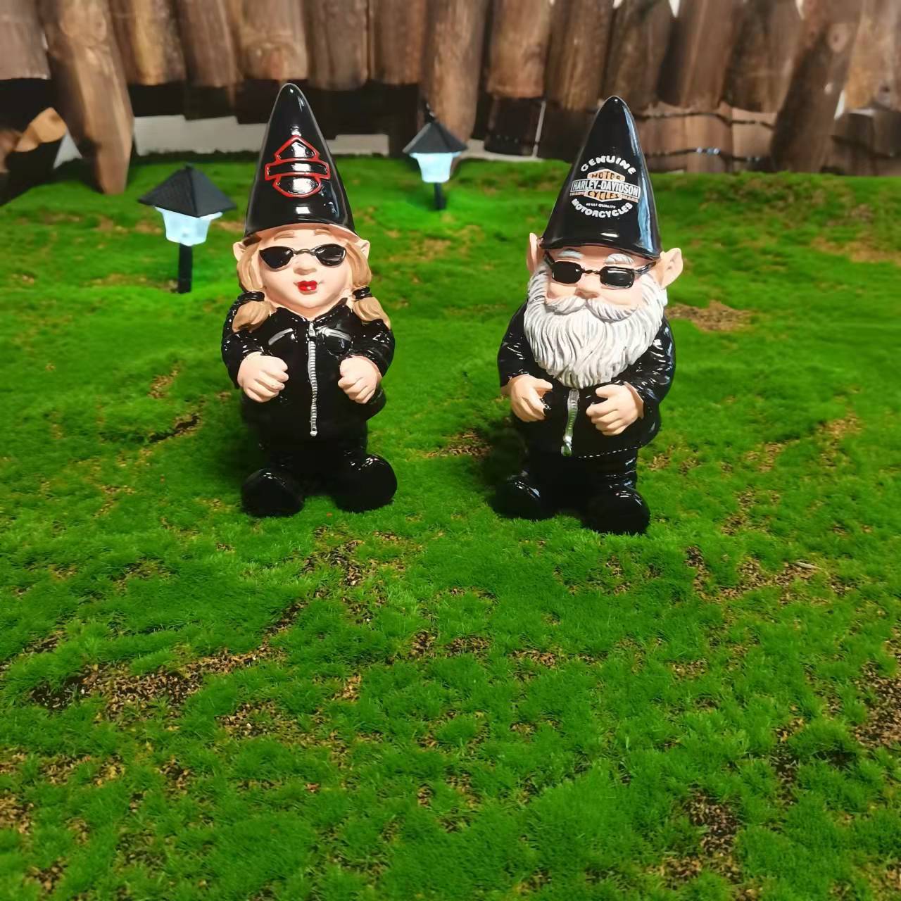 Two biker gnomes on a green moss lawn beside a wooden fence