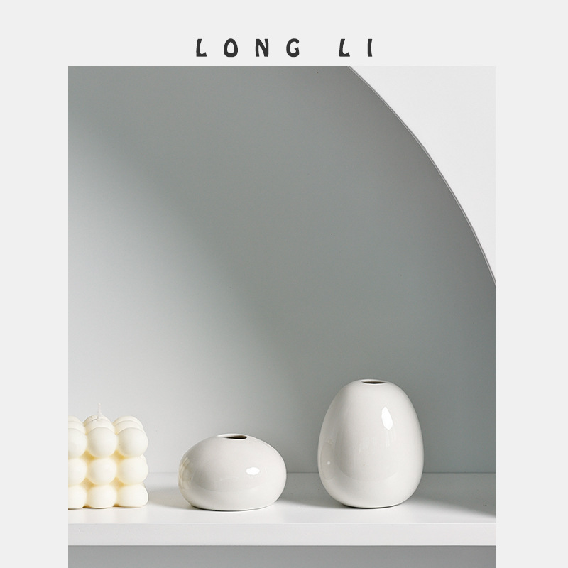 Two white ceramic vases beside a white bubble candle on a shelf