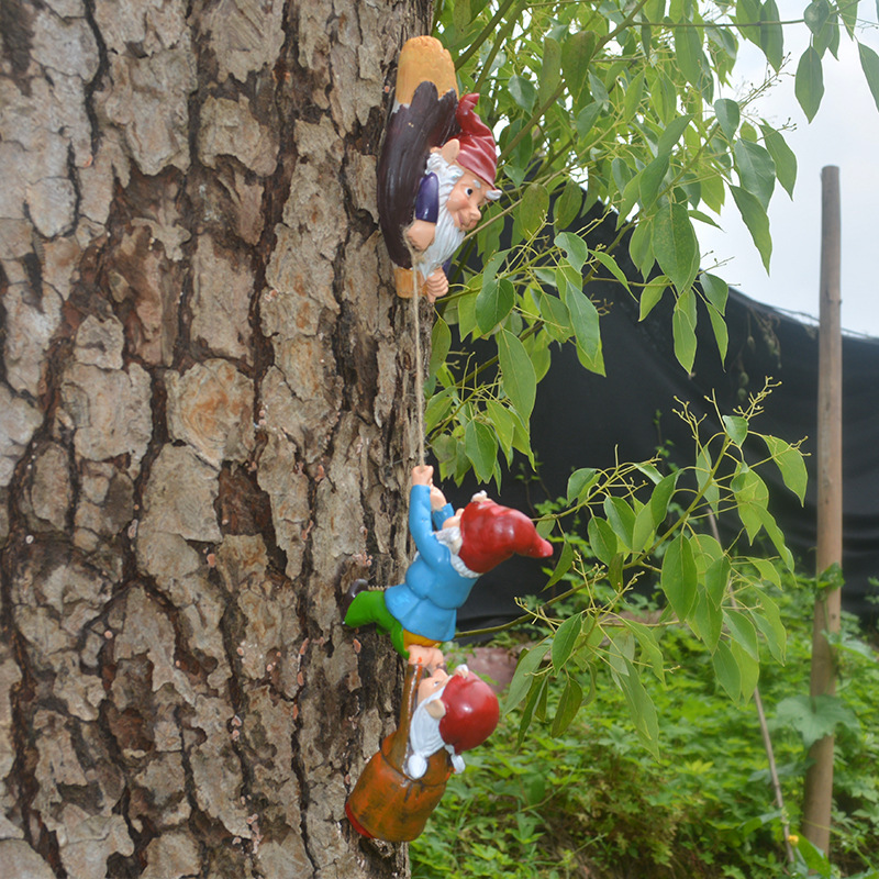 Gnome figurines climbing a rope on a pine tree among green foliage