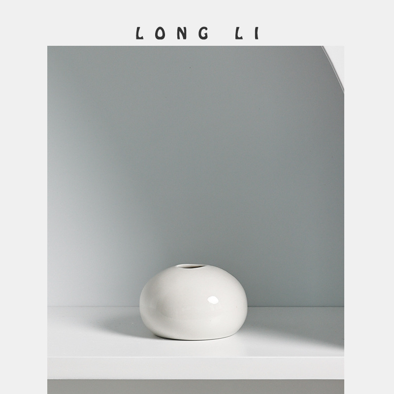 Close view of the round pebble-shaped white ceramic vase with glossy glaze