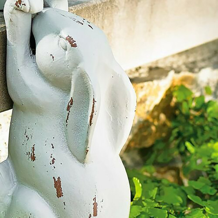 Rabbit peeking over a weathered stone wall edge with aged paint
