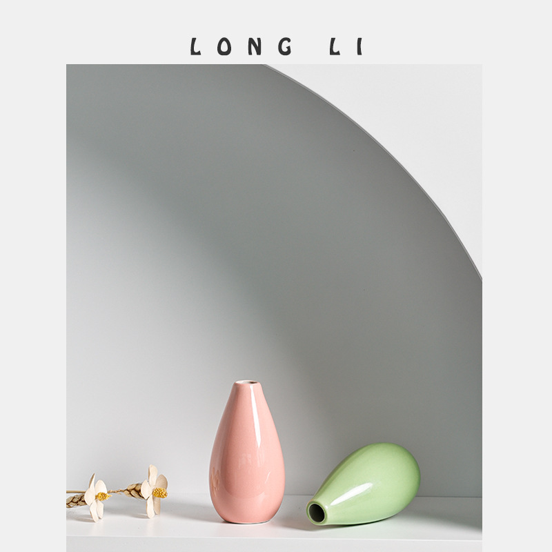 Pink vase upright beside a green vase on its side with dried flowers