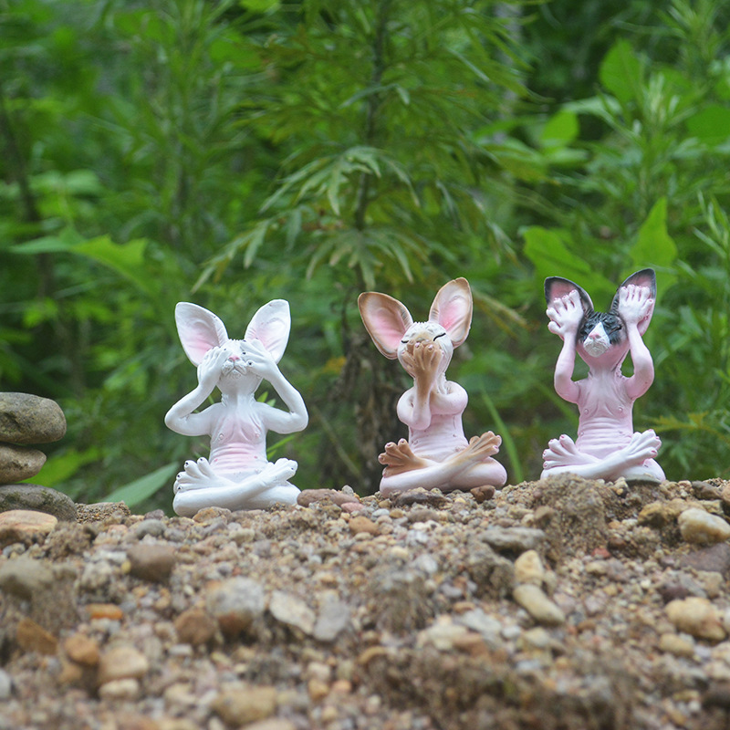 Resin meditating figurines sitting on pebbles in a green garden setting