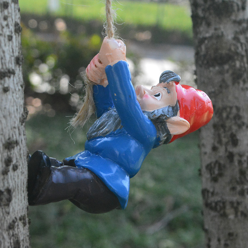 Climbing gnome dangling from rope against a blurred garden and tree backdrop