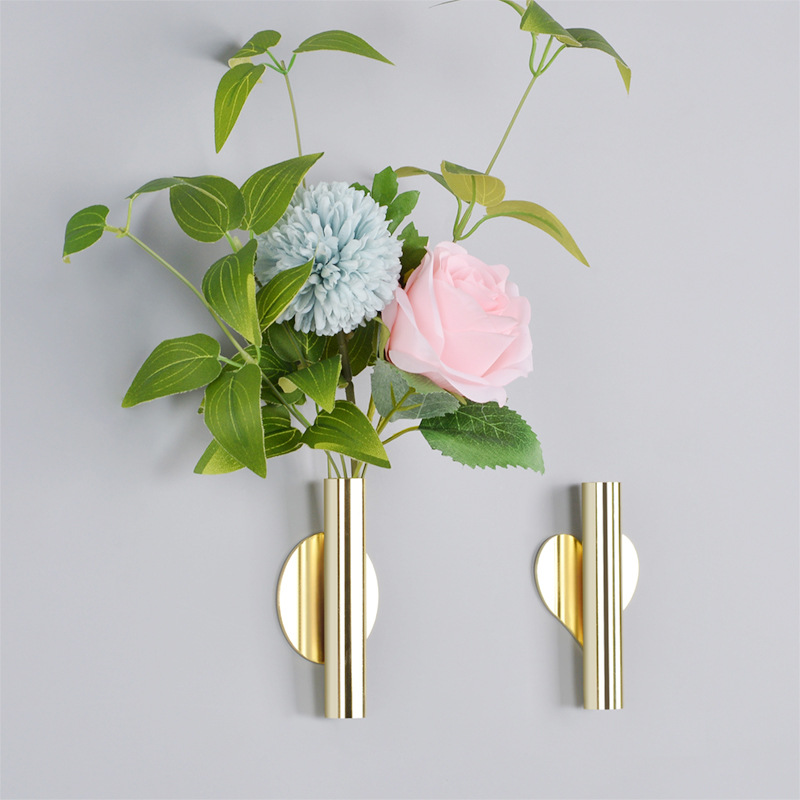 Gold wall vases holding artificial blue dahlia and pink rose on a grey wall