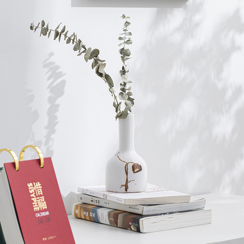 Bottle-neck white ceramic vase with brown branch holding eucalyptus on books