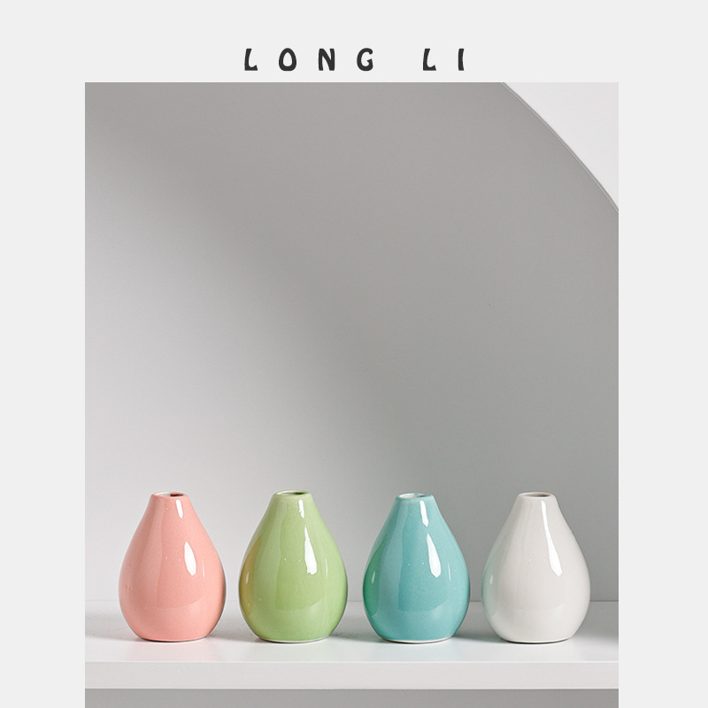Four mini ceramic vases in pink, green, teal and white lined up on a shelf
