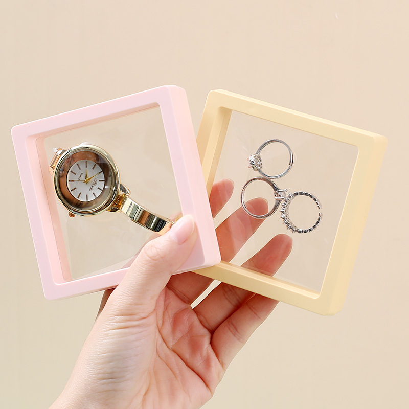 Hand holding a pink watch frame and a yellow ring frame against cream