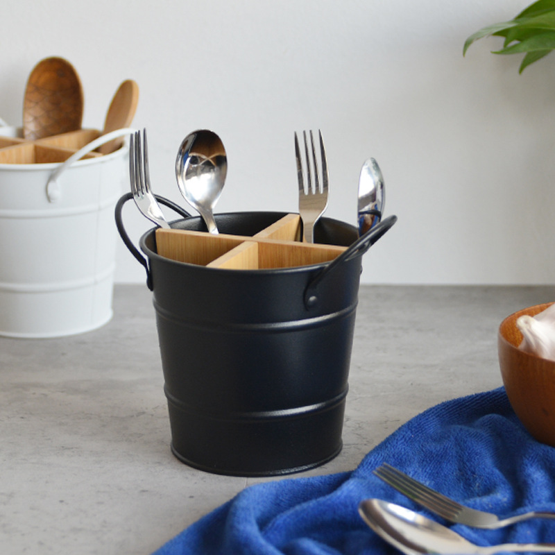 Black metal utensil bucket beside a white one on a grey countertop with cutlery