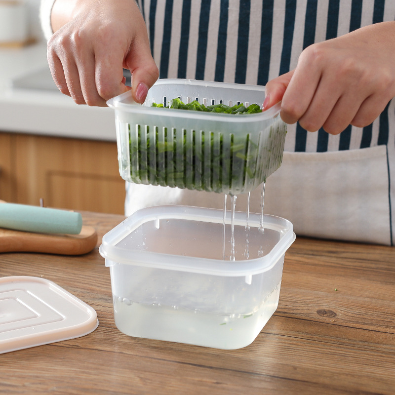 Hands lifting a slotted basket of greens above a clear base with water draining