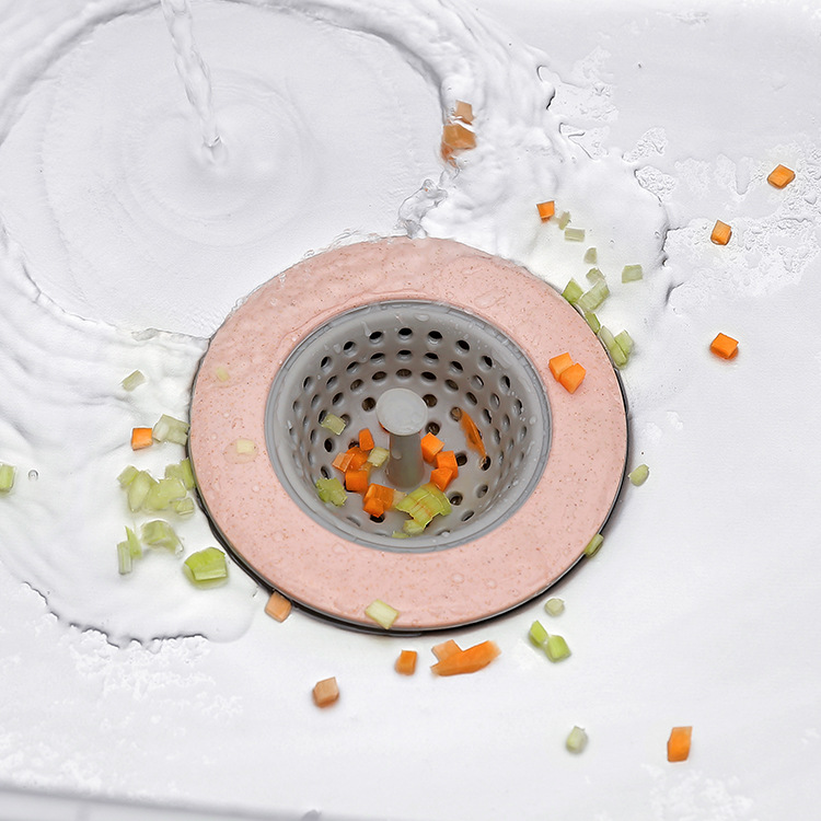 Pink sink strainer in a white sink with chopped carrot caught in the mesh