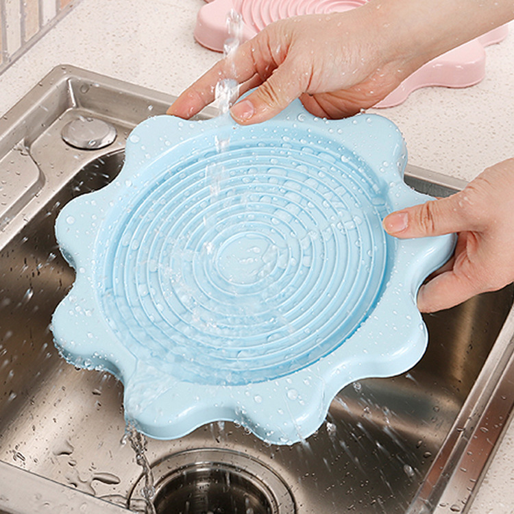 Hands rinsing a blue flower-shaped pad under running water in a steel sink