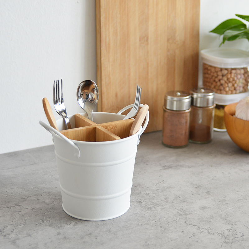 White metal utensil bucket with bamboo dividers holding forks, spoons and wooden-handled utensils