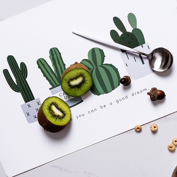 Cactus-print placemat beside sliced kiwi, acorns and a silver spoon
