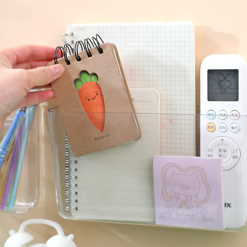 Hand reaching for a small notebook from a clear wall box beside a remote