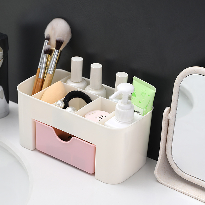 Cream organizer with pink drawer holding brushes beside a dressing table mirror