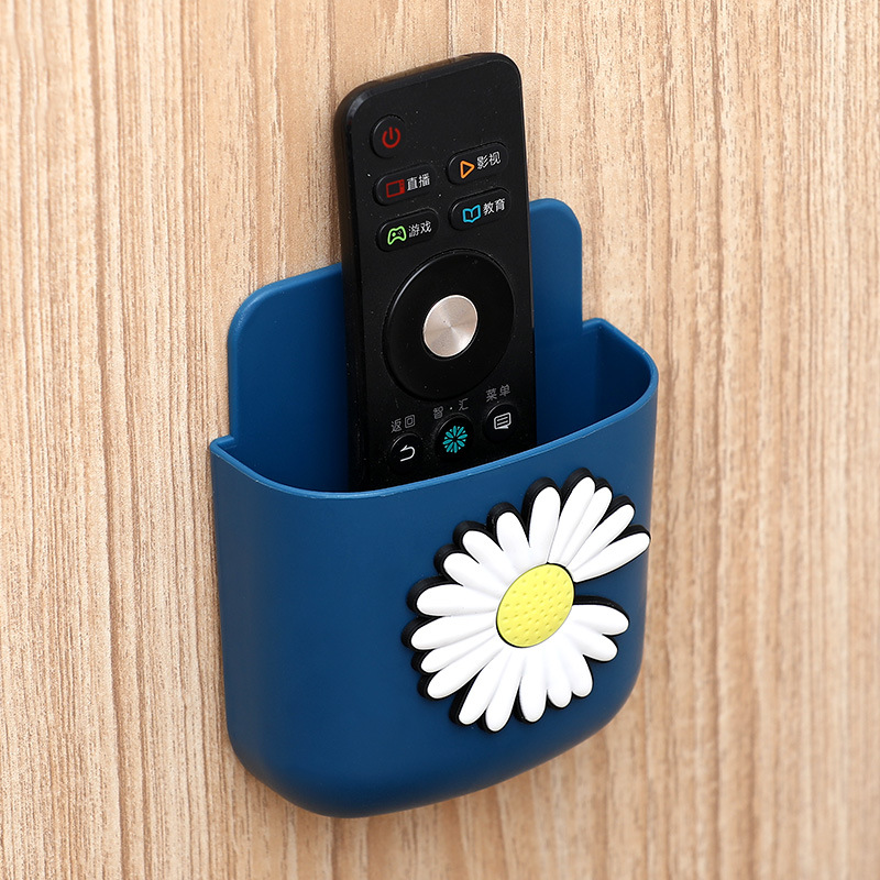 Navy daisy wall pocket holding a black TV remote on a wood-grain wall