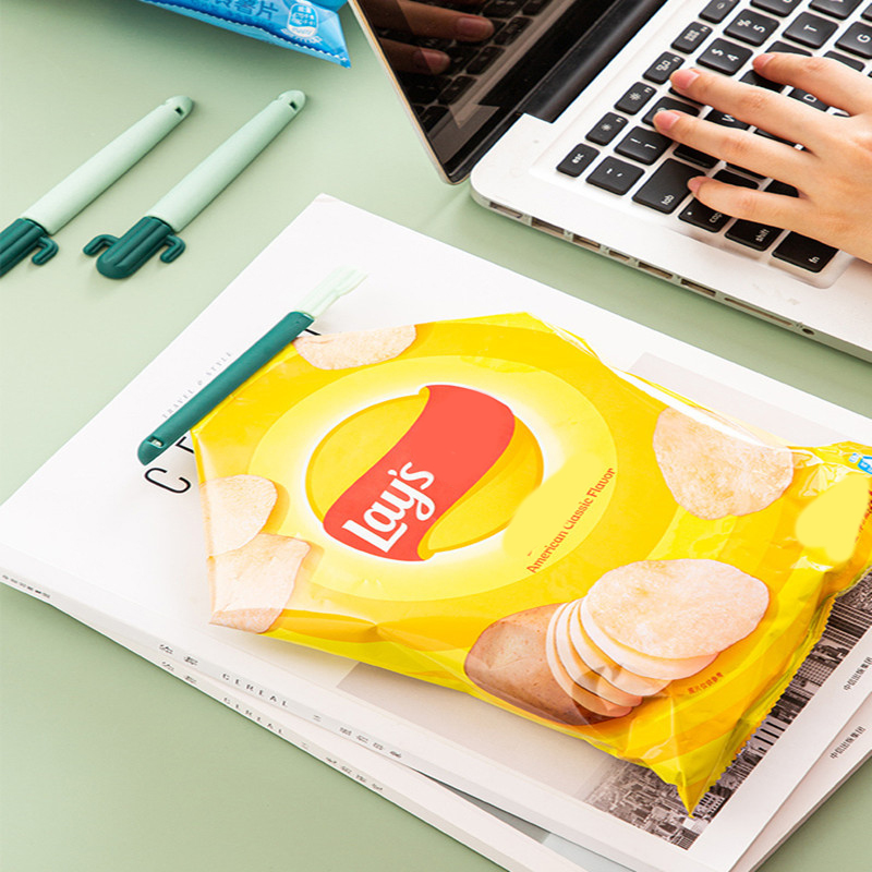 Cactus clip sealing a chip bag on a desk beside a laptop