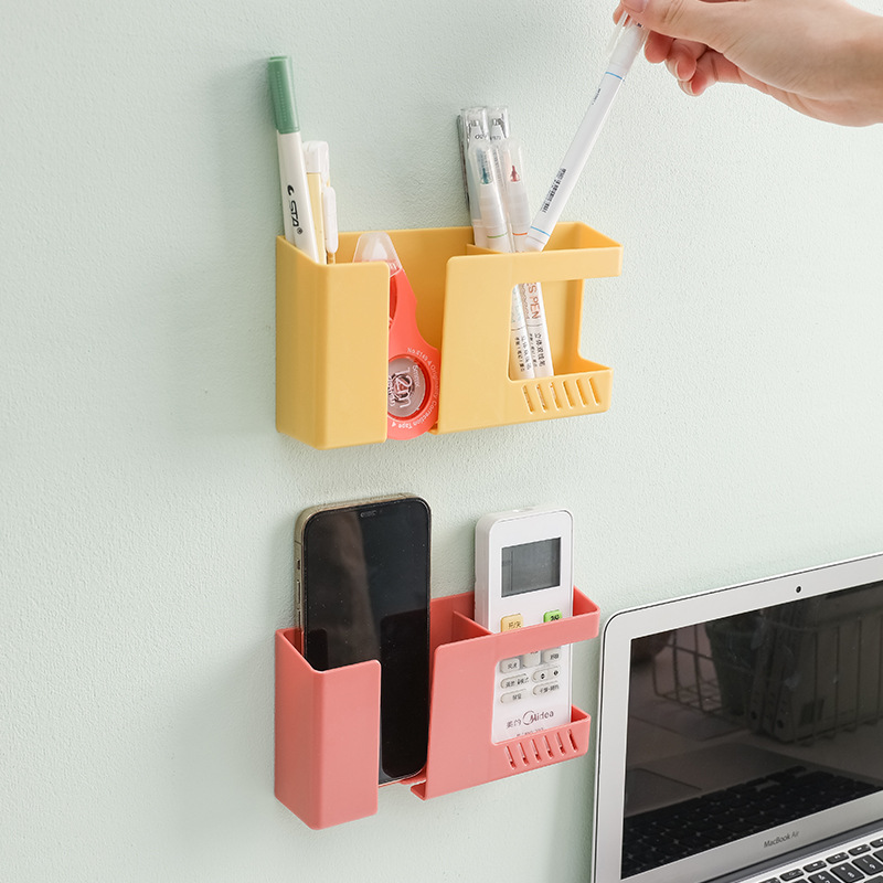 Mustard and coral wall caddies on a pale wall holding pens and a remote