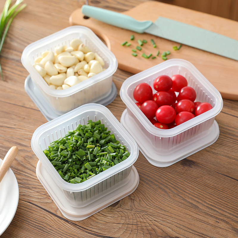 Clear storage boxes on a kitchen table holding garlic, green onions and tomatoes