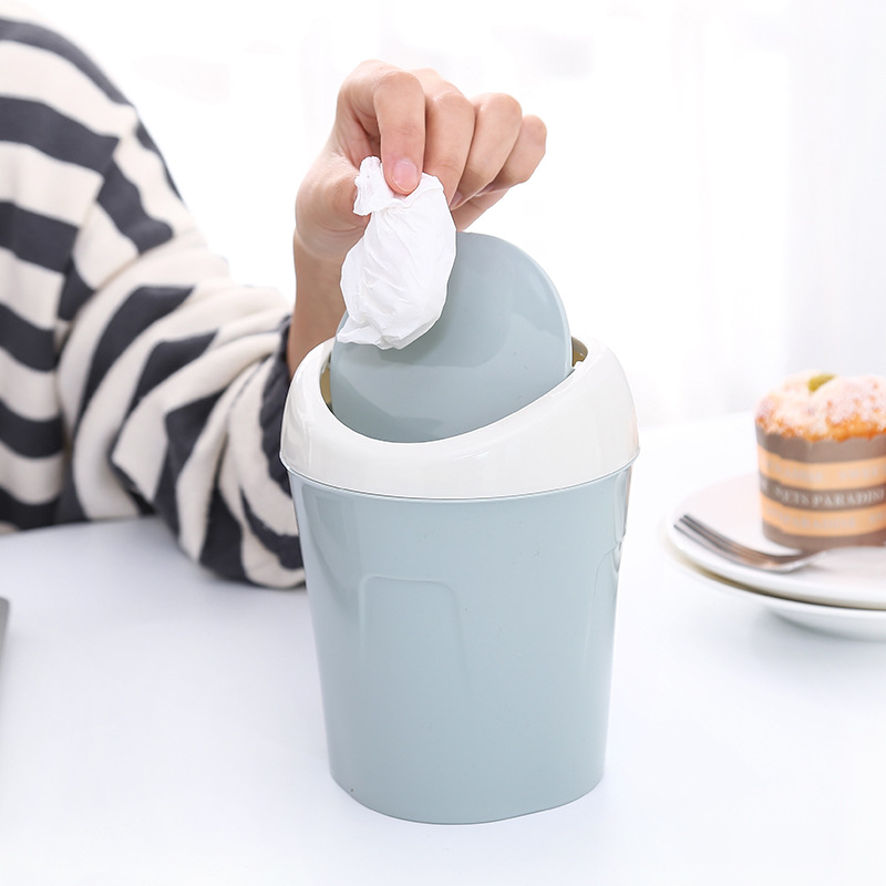 Hand dropping a crumpled tissue into a grey-blue mini trash can