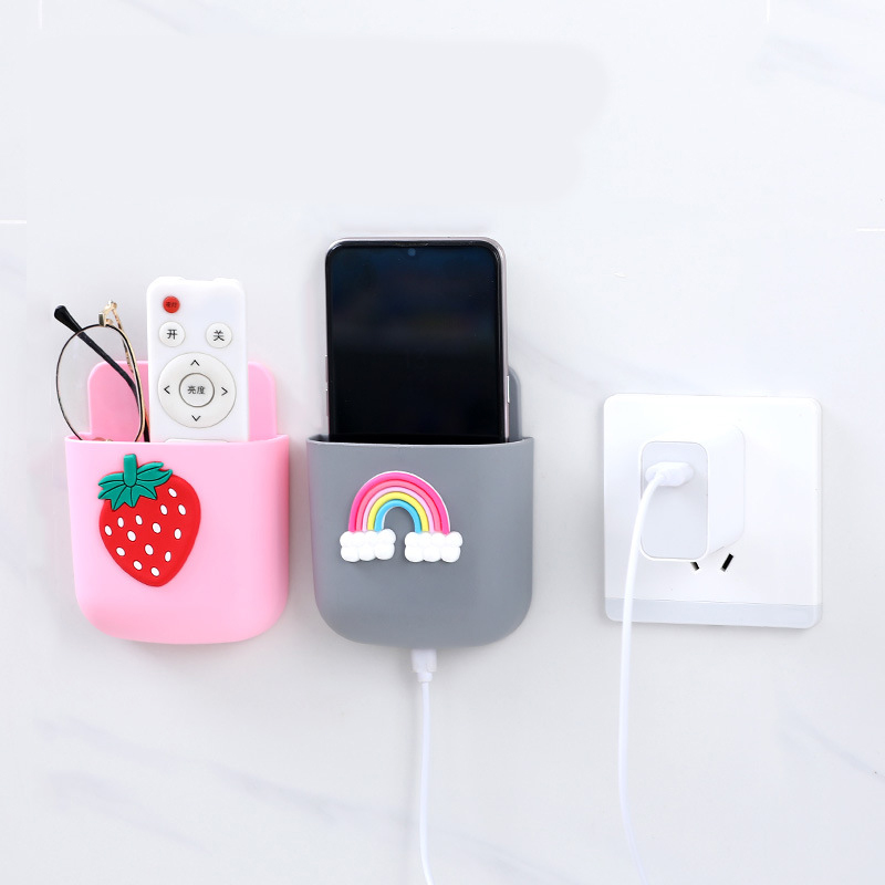 Pink strawberry pocket holding a TV remote and glasses on a white wall