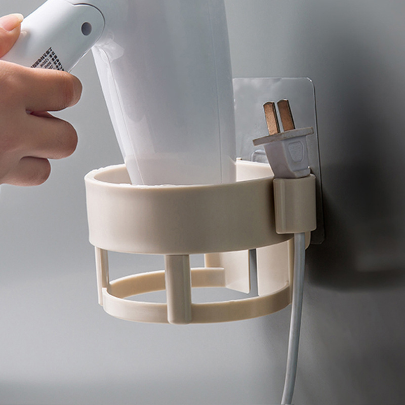 Hand lifting a hair dryer from a beige holder, cord clipped to the side