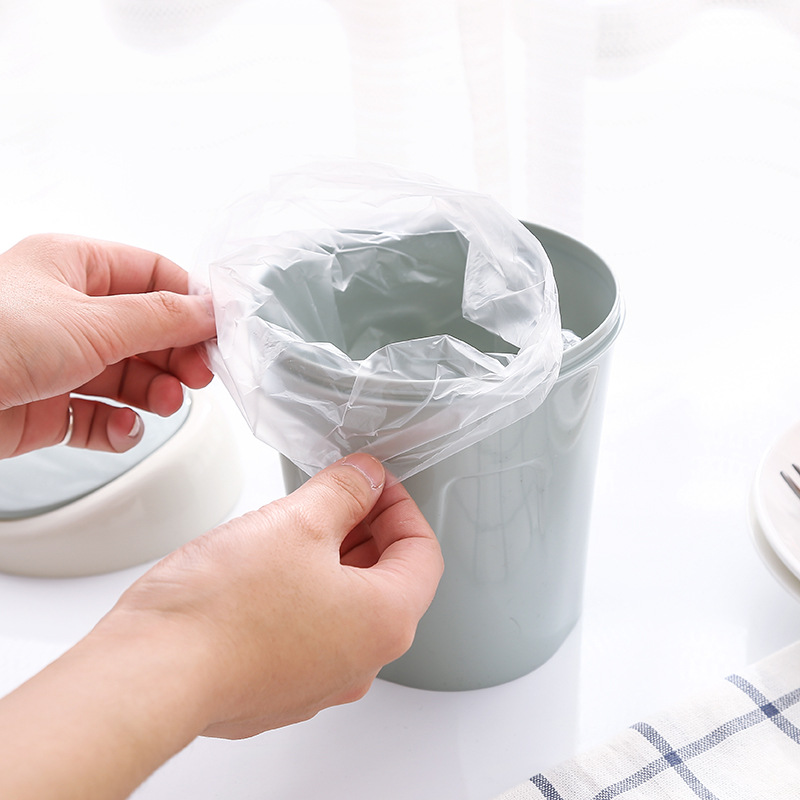 Hands fitting a clear plastic bag over the rim of a grey mini trash can