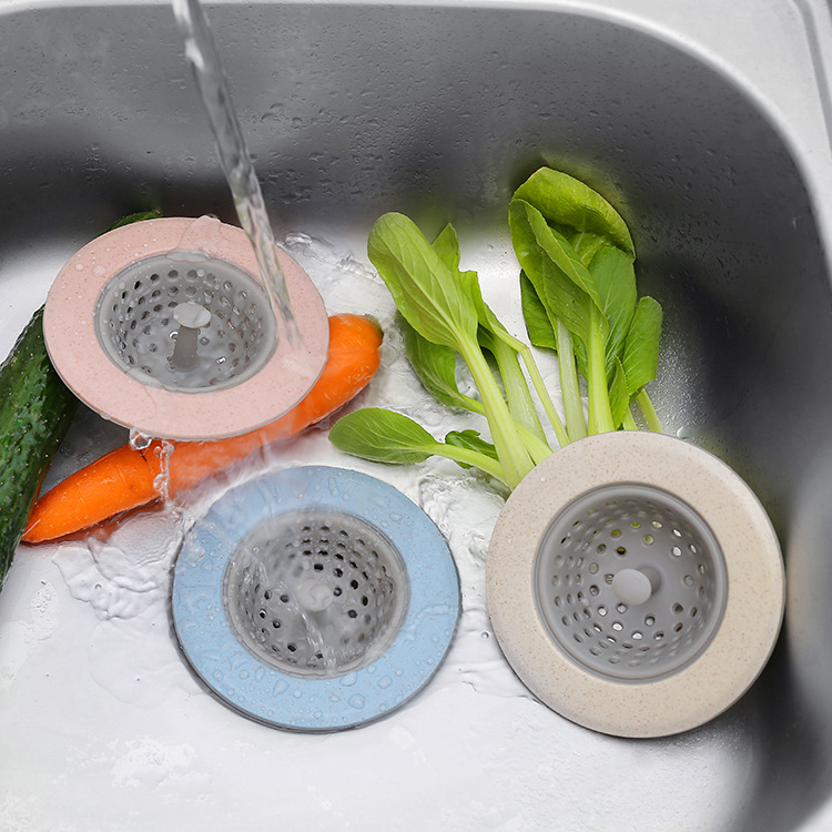 Blue, pink and beige sink strainers beside carrot and bok choy during rinsing
