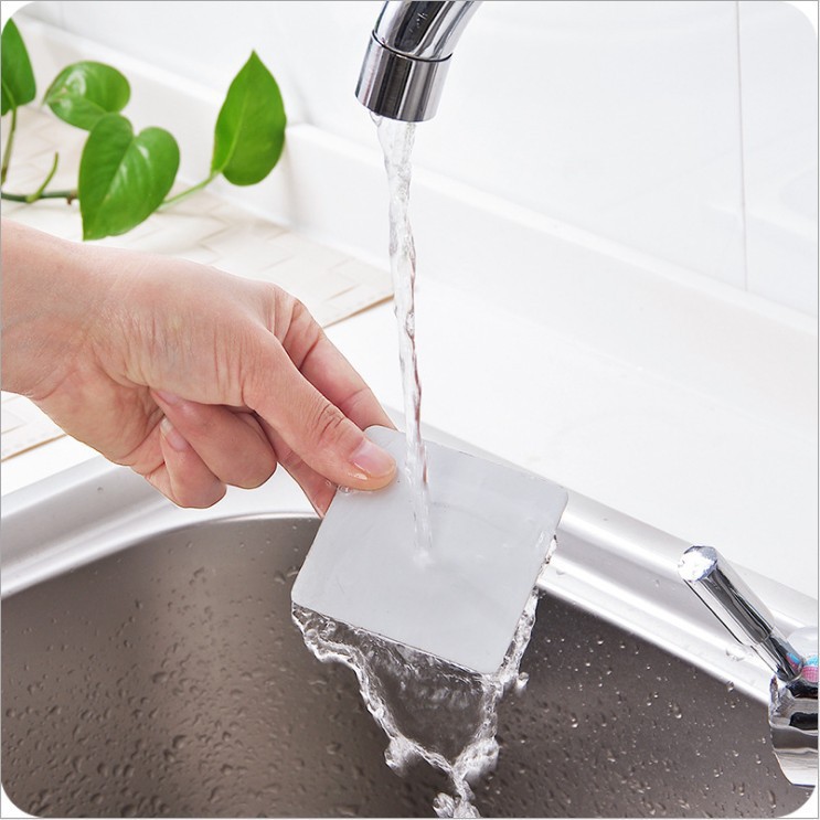 Hand pressing a punch-free adhesive plate onto wet tile under running water