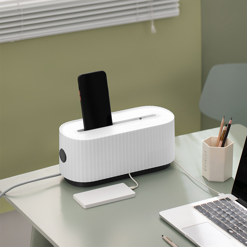White cable storage box with phone in top slot beside laptop and pen holder