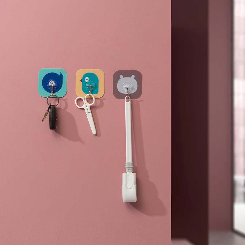 Pink wall with three cartoon hooks holding a key ring, scissors and a white tool