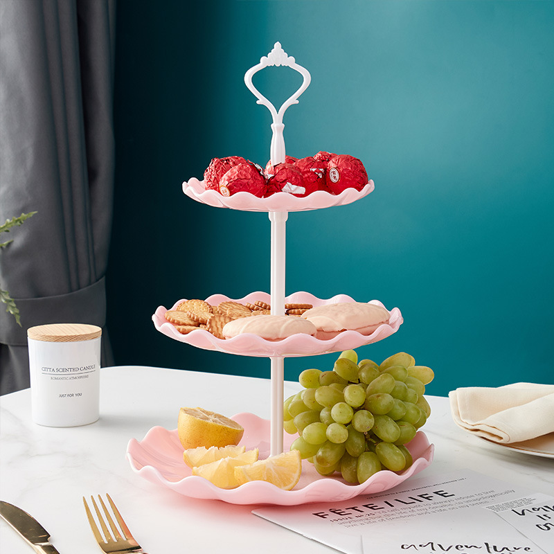 Pink three-tier stand with white handle holding candy, crackers, cookies and lemon