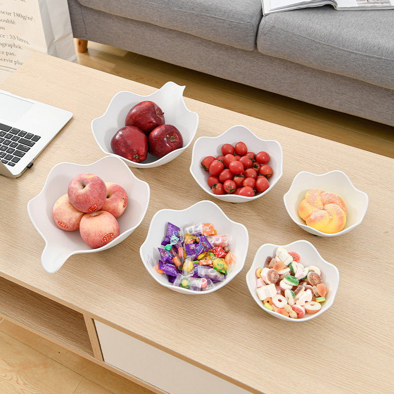 Six white petal-shaped bowls in varied sizes filled with apples, tomatoes and candy