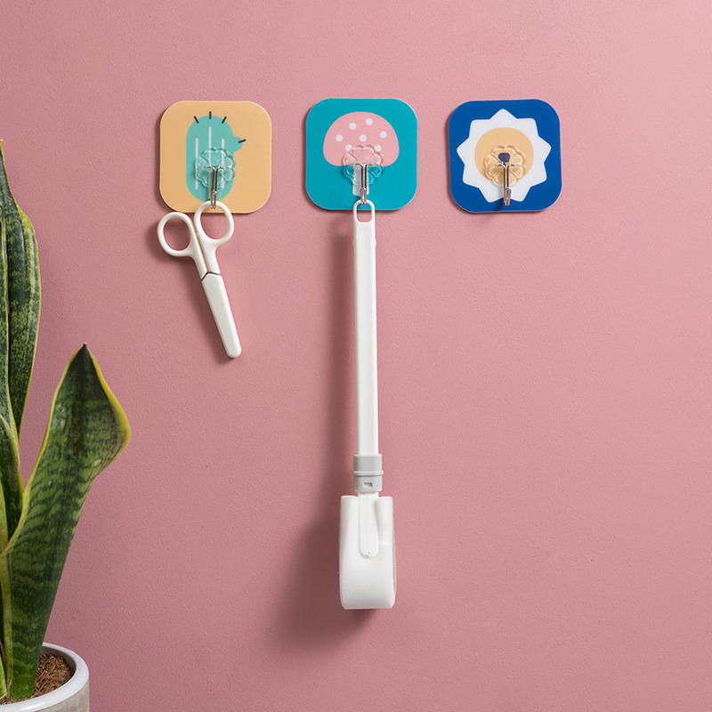 Pink wall with cartoon hooks holding scissors and a long white handheld tool