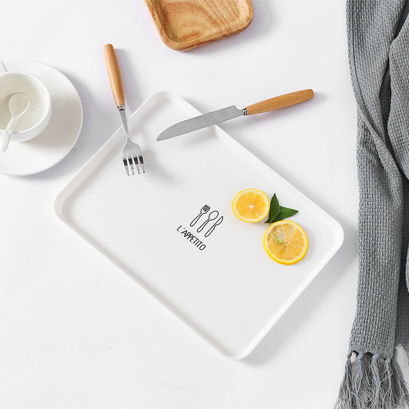 White rectangular plate with L'APPETITO cutlery print beside lemon slices